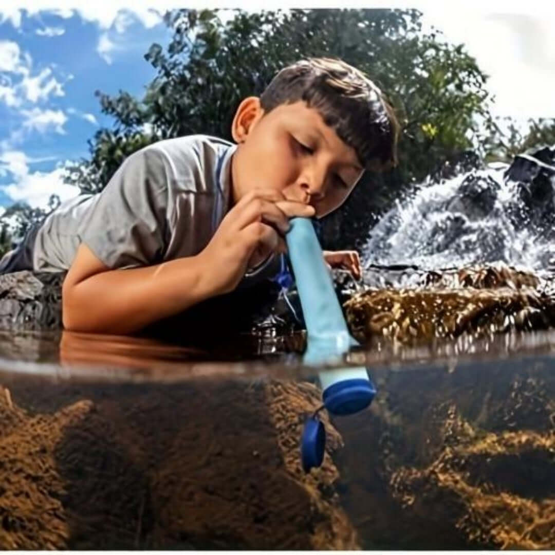 Child using Emergency Water Filter Straw to drink water from a stream in a natural outdoor setting.