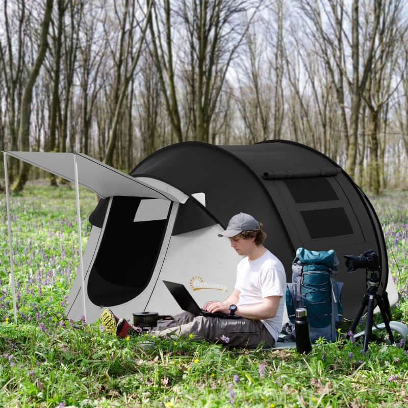 3-Person Pop Up Tent With Porch And Carry Bag set up in nature with man using laptop and camping gear.