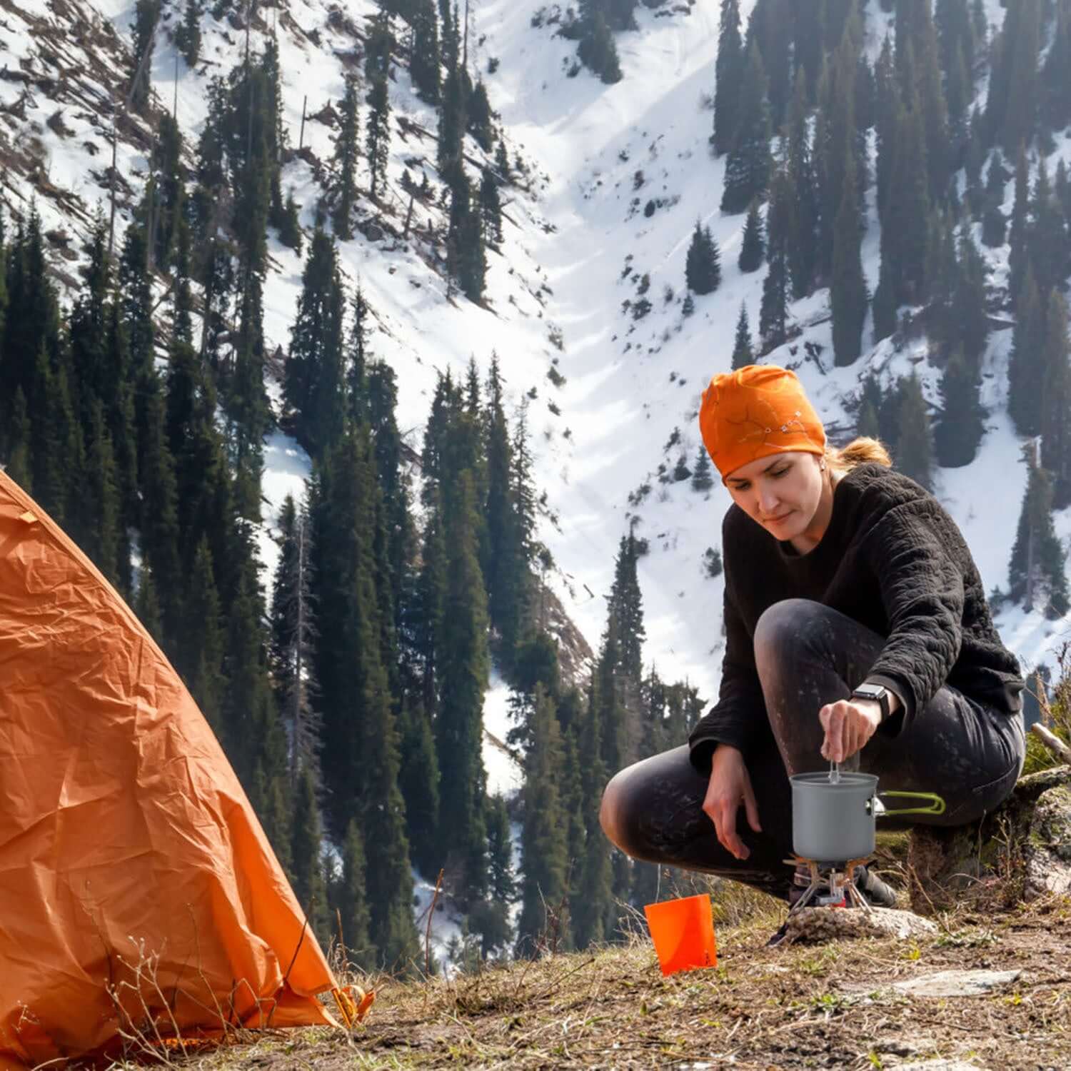 Person using 8pcs Camping Cookware Set outside a tent in a snow-covered mountain landscape.